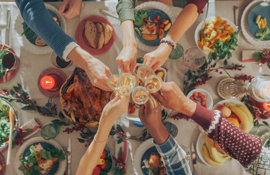 Изглед отгоре на празнично подредена зимна маса, на която няколко души вдигат наздравица с чаши.